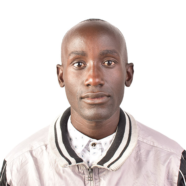 A close-up portrait of a young man with a shaved head, wearing a light purple jacket with a black and white collar and a white shirt, set against a plain white background.